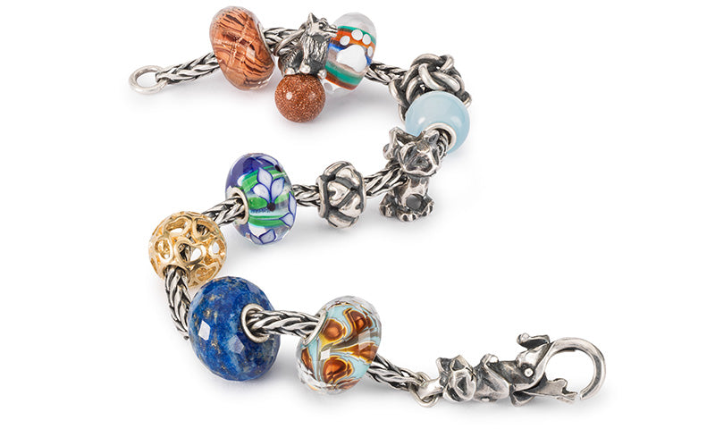 Trollbeads bracelet a mix og beads in gold, silver and gemstones, one glass bead with a small paw print charm, and beads with cats and a dog representing the cherished bond and affection between pets and their owners.